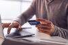 person holding a credit card and typing on a laptop